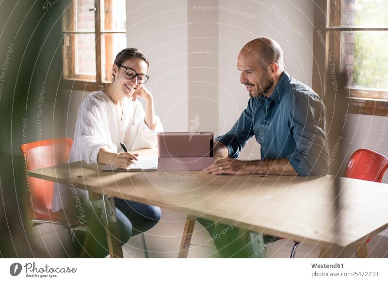 Businesswoman writing in notepad while sitting by man using digital tablet at office color image colour image indoors indoor shot indoor shots interior