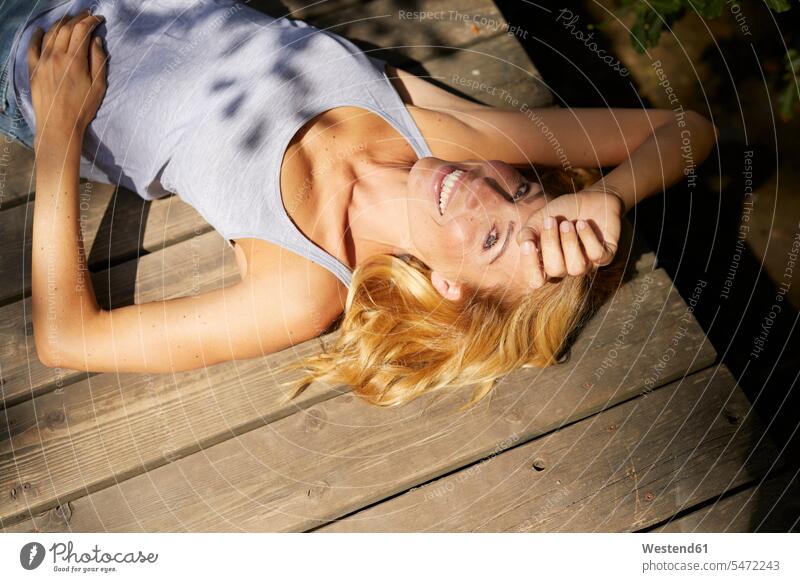 Happy blond woman lying on wooden jetty in sunshine sunlight Sunlit happiness happy laying down lie lying down jetties blond hair blonde hair females women