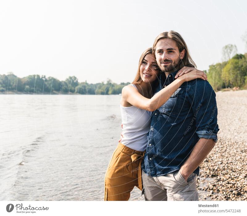 Happy young couple in love embracing at the riverside River Rivers riverbank happiness happy twosomes partnership couples embrace Embracement hug hugging water