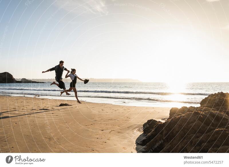 France, Brittany, happy young couple jumping on the beach at sunset happiness twosomes partnership couples Leaping beaches people persons human being humans