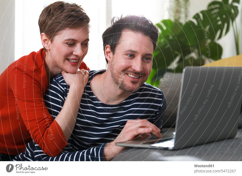 Couple sitting at home, using laptop couple twosomes partnership couples Laptop Computers laptops notebook using a laptop Using Laptops woman females women