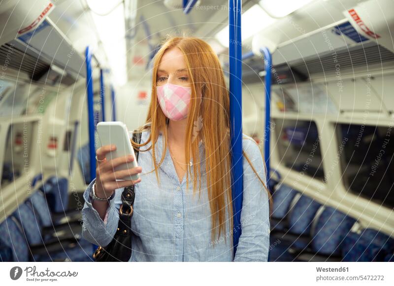 Young woman in mask using smart phone while standing in train color image colour image Train Interior railway railroad Railways railroads transportation