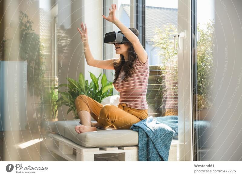 Young woman sitting at the window at home wearing VR glasses females women virtual specs Eye Glasses spectacles Eyeglasses Seated windows Adults grown-ups