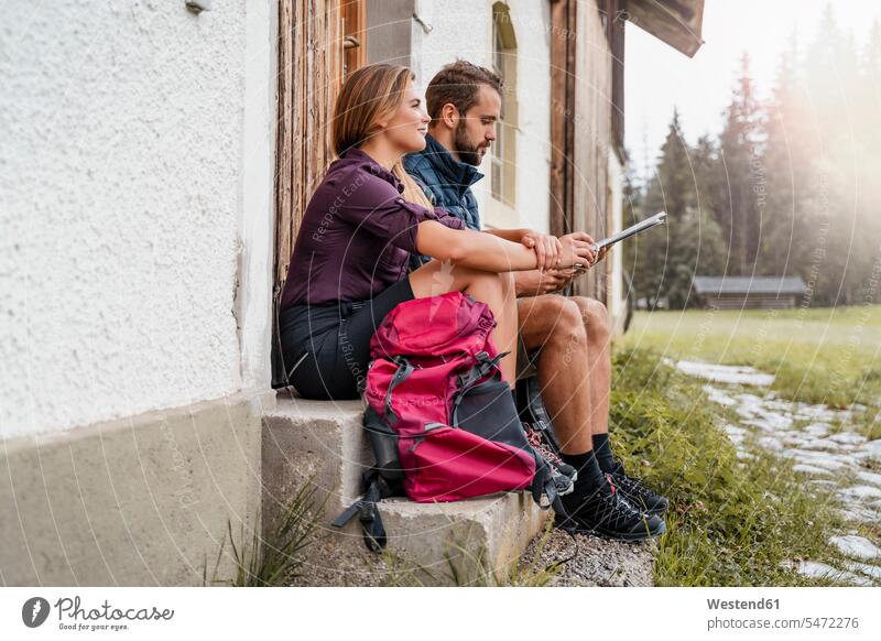Young couple with map at a farmhouse during a hiking trip, Vorderriss, Bavaria, Germany touristic tourists back-pack back-packs backpacks rucksack rucksacks