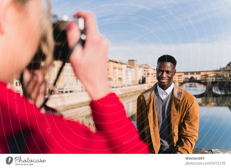 Young woman taking a picture of her boyfriend on a bridge above river Arno, Florence, Italy human human being human beings humans person persons African black