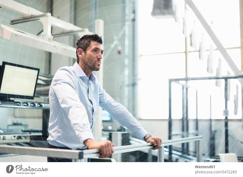 Businessman standing at railing in factory thinking Business man Businessmen Business men Railing Railings factories business people businesspeople