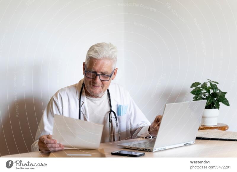 Smiling doctor looking at medical record while sitting against wall color image colour image indoors indoor shot indoor shots interior interior view Interiors