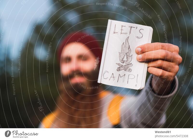 Bearded man in a forest holding 'Let's Camp' sign men males camping woods forests signs beard Adults grown-ups grownups adult people persons human being humans