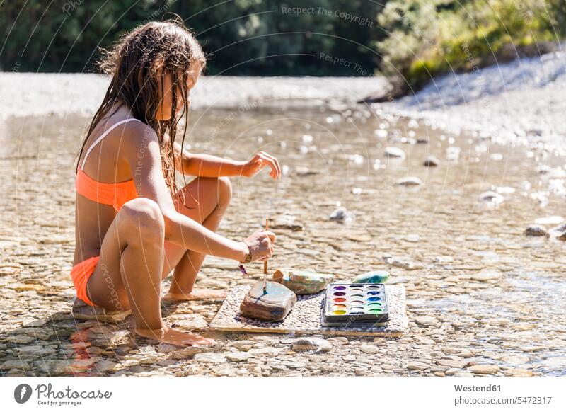 Girl sitting in water of a river painting on stone Seated girl females girls stones River Rivers child children kid kids people persons human being humans