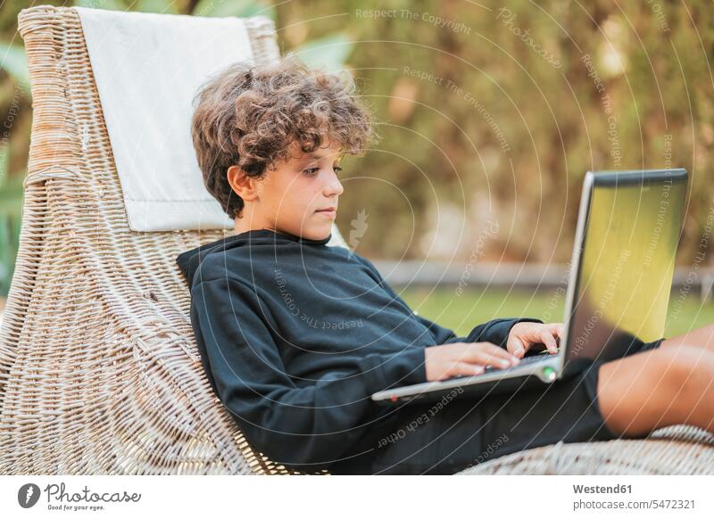 Relaxed boy using laptop on lounge in garden human human being human beings humans person persons caucasian appearance caucasian ethnicity european