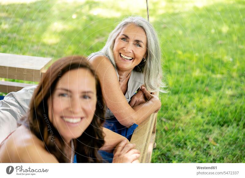Portrait of two happy women relaxing on a hanging bed in garden relaxed relaxation happiness beds portrait portraits woman females female friends gardens