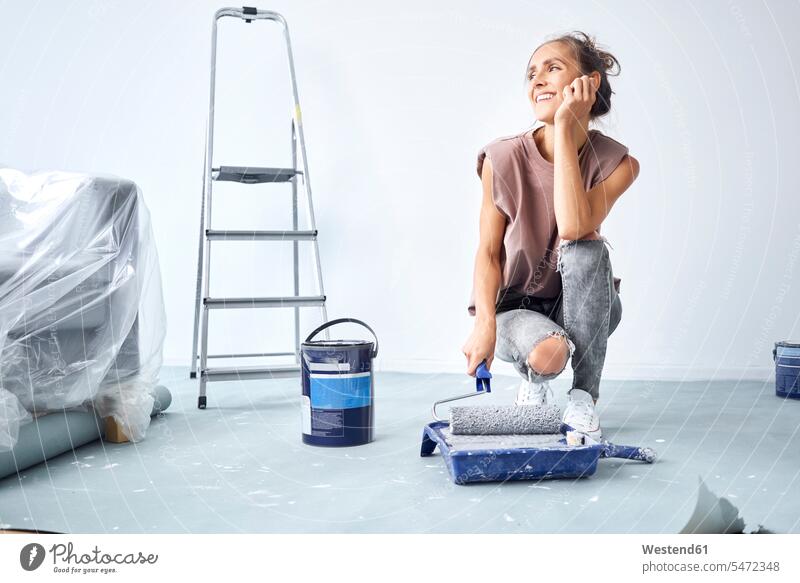 Young woman head in hands holding paint roller in paint tray while crouching at home color image colour image indoors indoor shot indoor shots interior