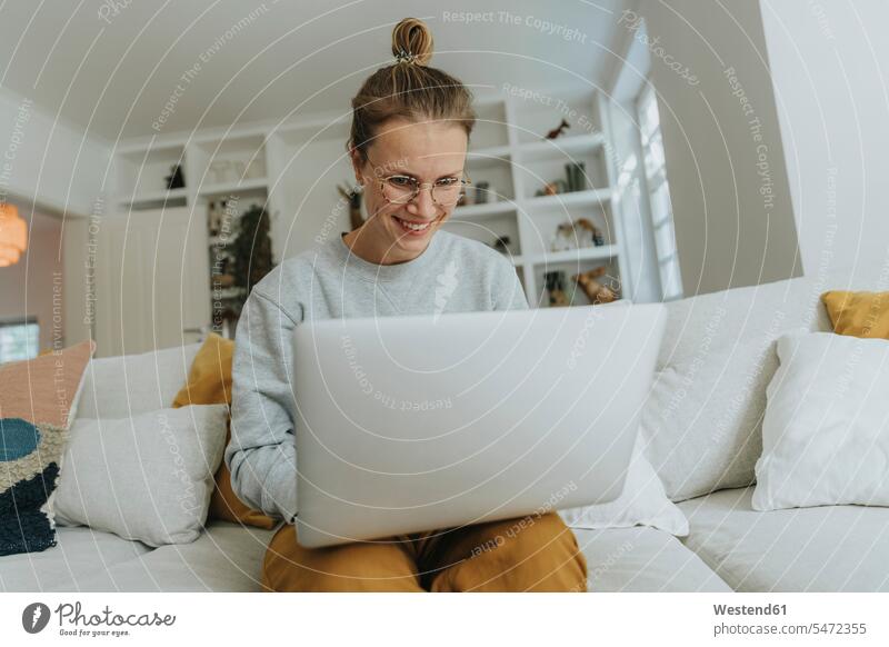 Smiling woman working on laptop while sitting on sofa at home color image colour image indoors indoor shot indoor shots interior interior view Interiors day