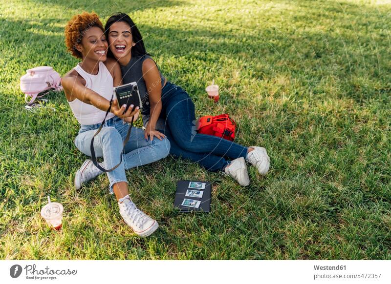 Two happy female friends taking an instant photo in a park parks happiness instant photography polaroid polaroids instant photos relaxed relaxation photographs
