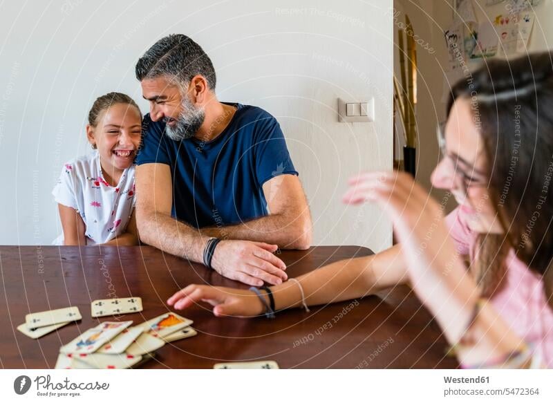Happy father with two daughters playing cards on wooden table at home T- Shirt t-shirts tee-shirt Tables wood table games parlor games parlour game