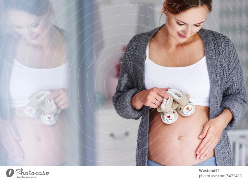 Pregnant woman with baby booties smiling smile females women portrait portraits children's room Kids Room nursery child's room stroking petting pregnant