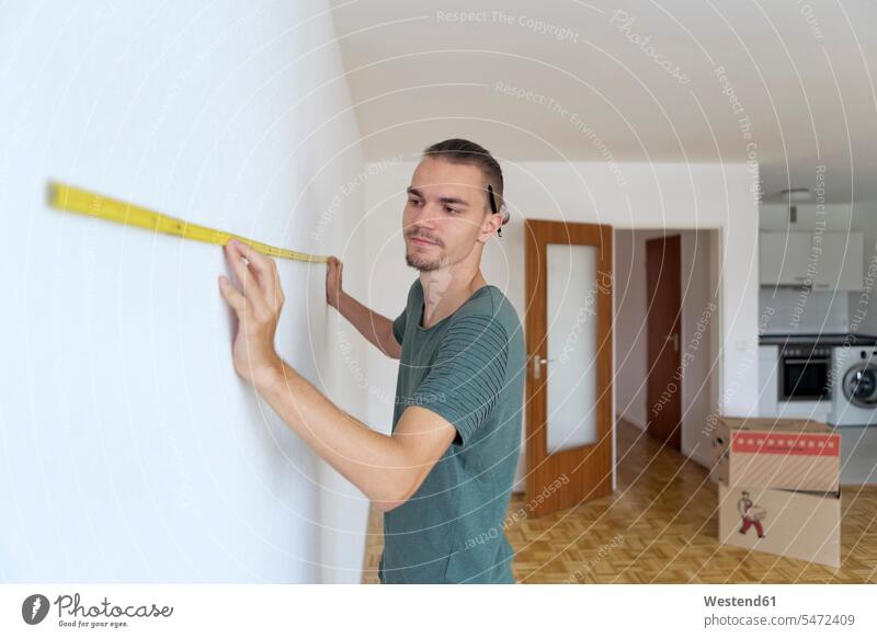 Young man measuring the wall in an empty apartment apartments flat flats human human being human beings humans person persons caucasian appearance