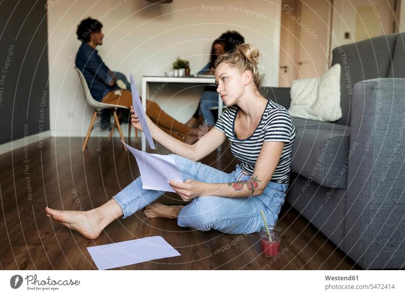 Young woman sitting on floor with papers and friends in background documents floors females women Seated Adults grown-ups grownups adult people persons