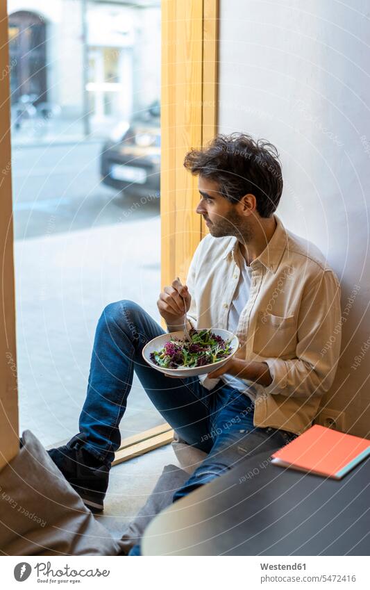 Man eating a salad sitting at the window in a restaurant looking out human human being human beings humans person persons celibate celibates singles
