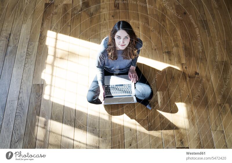 Portrait of young woman using laptop on wooden floor females women Laptop Computers laptops notebook wooden floors portrait portraits Adults grown-ups grownups