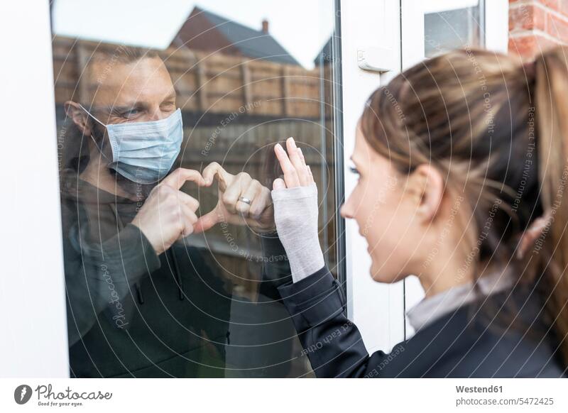 Boyfriend show heart shape gesture to girlfriend through window glass while quarantined at home color image colour image day daylight shot daylight shots