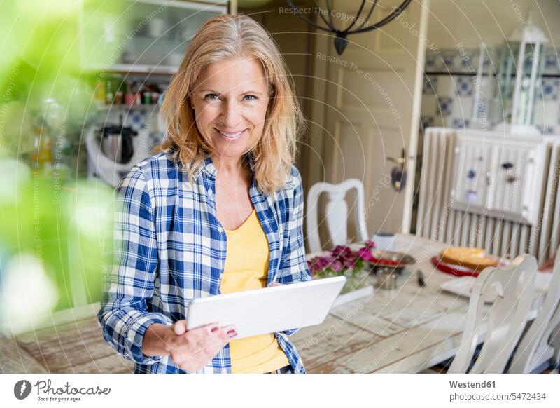 Portrait of smiling mature woman with digital tablet in the kitchen Tables Dining Tables Dinner Table wood wood table at home free time leisure time Lifestyle