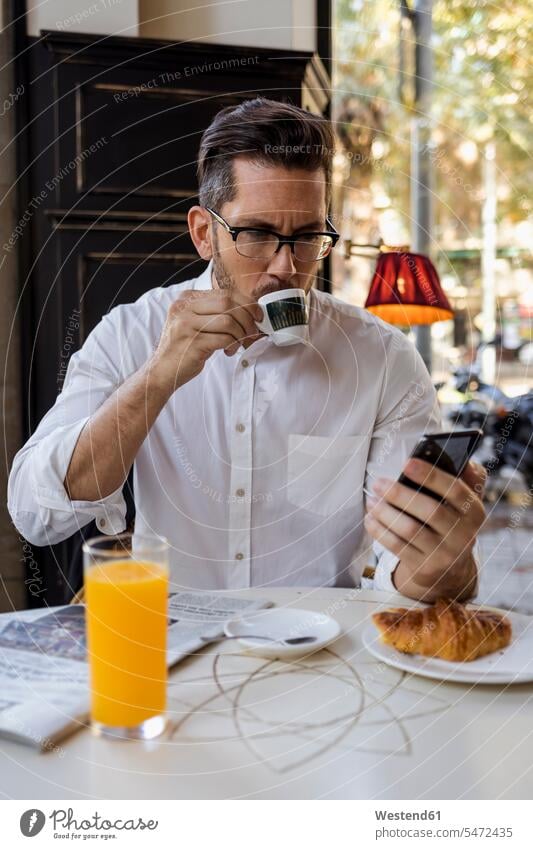 Businessman having breakfast in a cafe and checking cell phone Business man Businessmen Business men mobile phone mobiles mobile phones Cellphone cell phones
