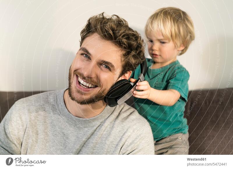 Happy father and son with headphones on couch at home happiness happy pa fathers daddy dads papa putting on settee sofa sofas couches settees sons manchild
