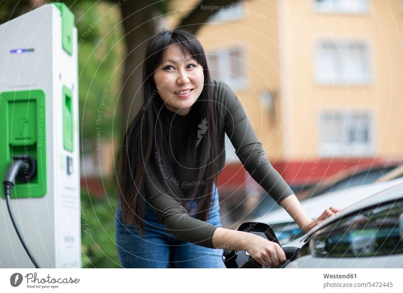 Carsharing, woman charging an electric car smile fuel fueling refuel refueling refuelling delight enjoyment Pleasant pleasure happy content Contented Emotion