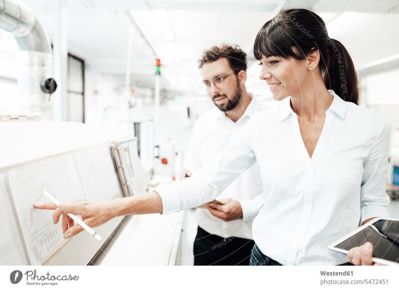 Smiling female technician pointing at graph while discussing with male colleague at laboratory color image colour image Germany indoors indoor shot indoor shots