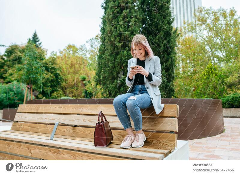 Smiling woman sitting on park bench using cell phone business life business world business person businesspeople business woman business women businesswomen