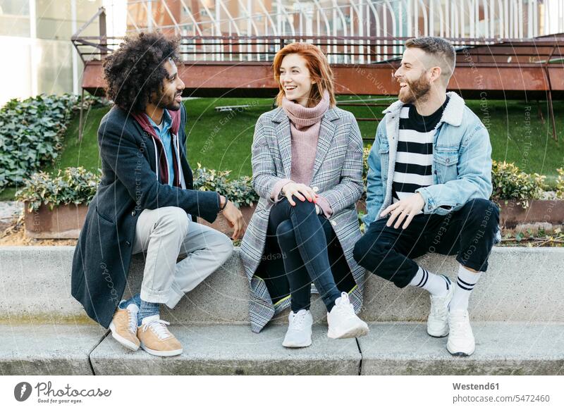 Three happy friends sitting in the city talking town cities towns Seated speaking happiness outdoors outdoor shots location shot location shots friendship