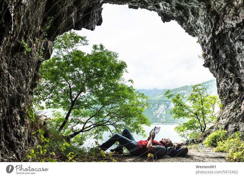 Mature man reading book while lying at cave entrance by Lake Como color image colour image Lario Lago di Como Como Lake Lombardy Italy indoors indoor shot