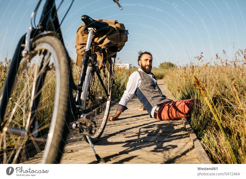 Well dressed man sitting on a wooden walkway in the countryside next to a bike human human being human beings humans person persons caucasian appearance