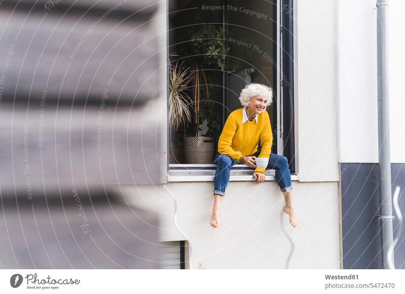 Mature woman holding coffee cup while sitting on window color image colour image outdoors location shots outdoor shot outdoor shots day daylight shot