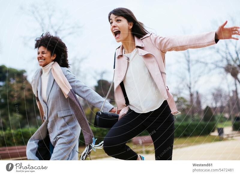 Spain, Barcelona, two exuberant women running in city park woman females exuberance hilarity Frolic parks town cities towns happiness happy female friends