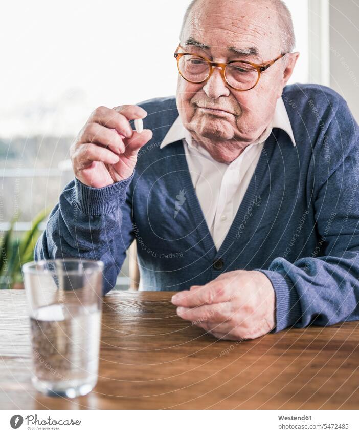 Portrait of senior man sitting at table with pill and glass of water Water senior men elder man elder men senior citizen portrait portraits Seated tablet Drink