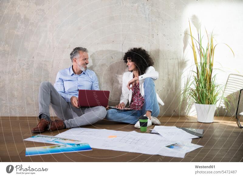 Businessman and businesswoman sitting on the floor in a loft working with laptop and documents Laptop Computers laptops notebook Seated floors Business man