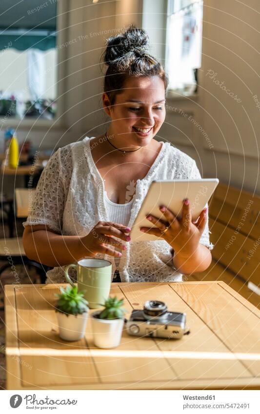 Smiling young woman using digital tablet while sitting at table in coffee shop color image colour image indoors indoor shot indoor shots interior interior view