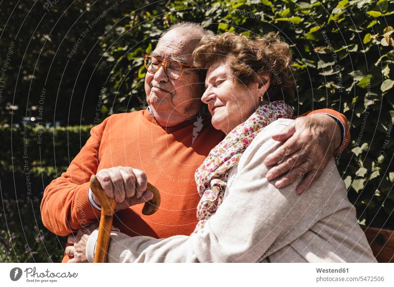 Senior couple sitting on bench in a park, with arms around parks summer summer time summery summertime senior couple elder couples senior couples Seated leaning