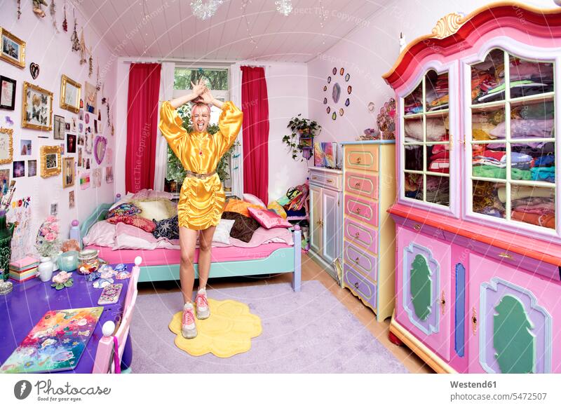 Young woman with hand raised sticking out tongue standing in flashy bedroom color image colour image indoors indoor shot indoor shots interior interior view