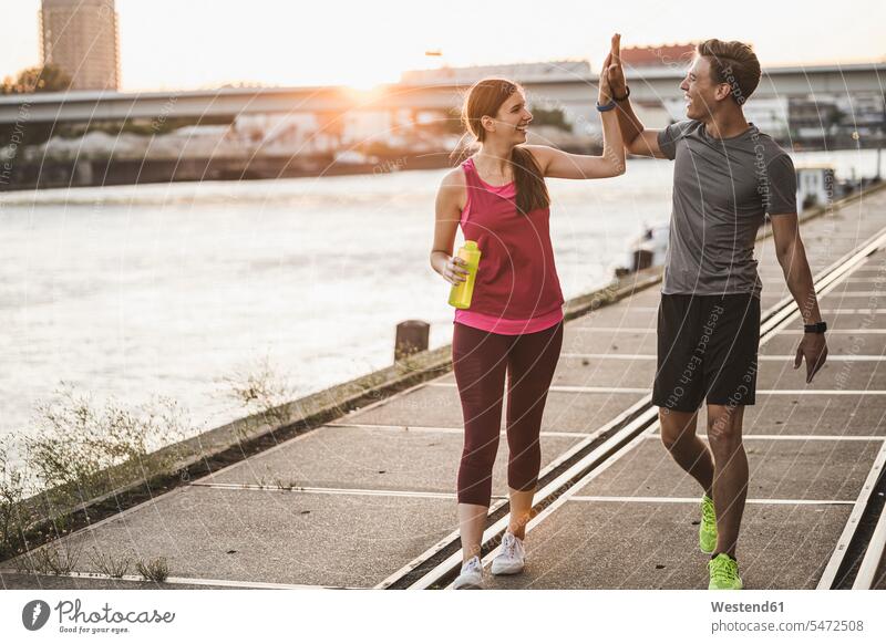 Smiling friends giving high-five while walking at harbor color image colour image outdoors location shots outdoor shot outdoor shots Sportswear Sports Wear