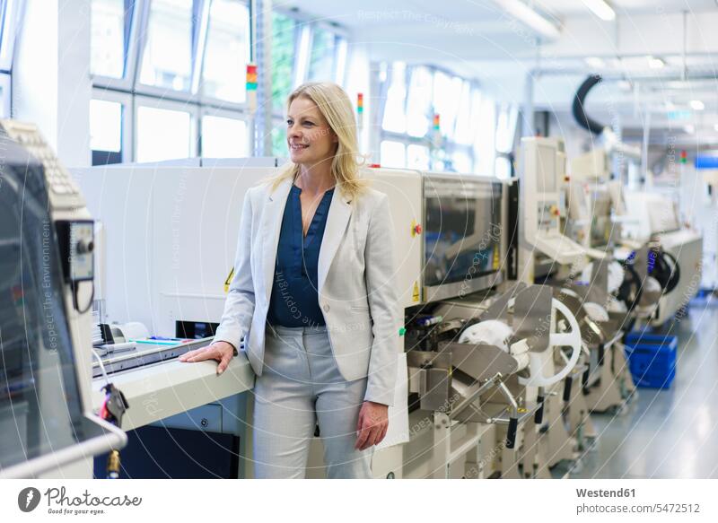 Thoughtful mature blond businesswoman standing by machinery while looking away at illuminated industry color image colour image indoors indoor shot indoor shots