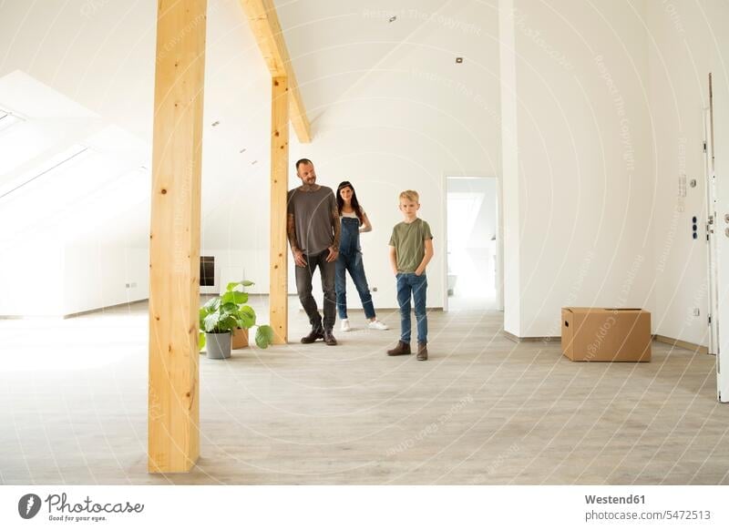 Parents with son standing on hardwood floor in attic of new unfurnished home color image colour image Germany indoors indoor shot indoor shots interior