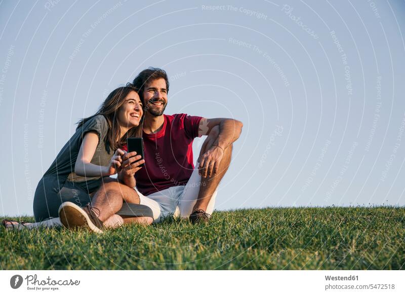 Couple sitting on grass against clear sky during sunset color image colour image outdoors location shots outdoor shot outdoor shots sunsets sundown atmosphere