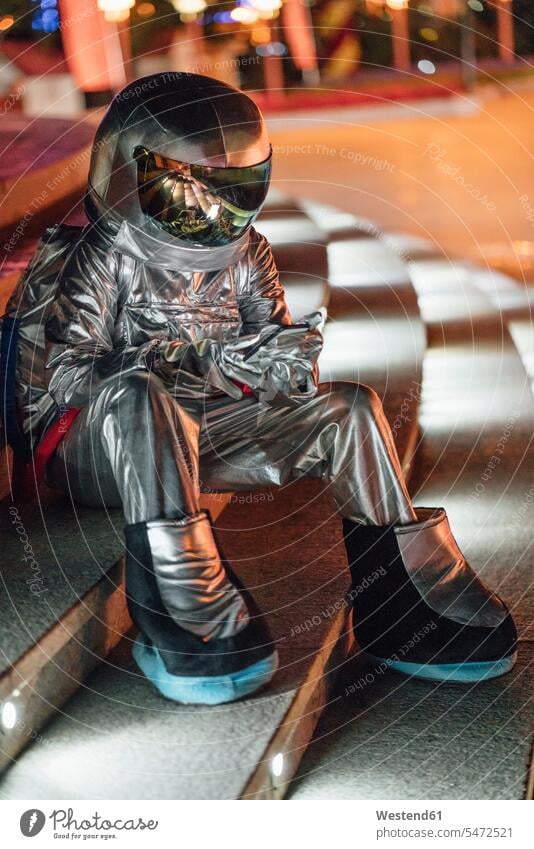 Spaceman sitting on illuminated stairs at night using cell phone astronaut astronauts spaceman spacemen lit lighted Illuminating mobile phone mobiles
