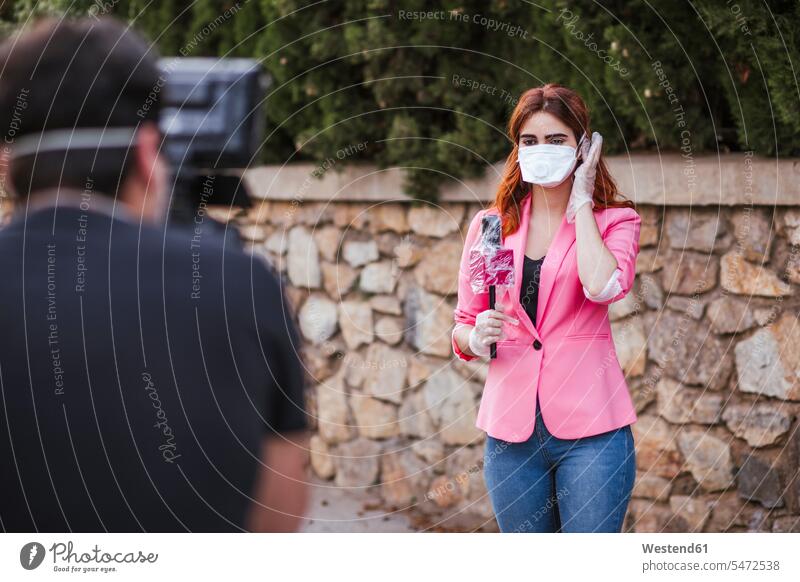 Camera operator filming reporter with microphone wearing mask while standing against wall color image colour image Spain day daylight shot daylight shots