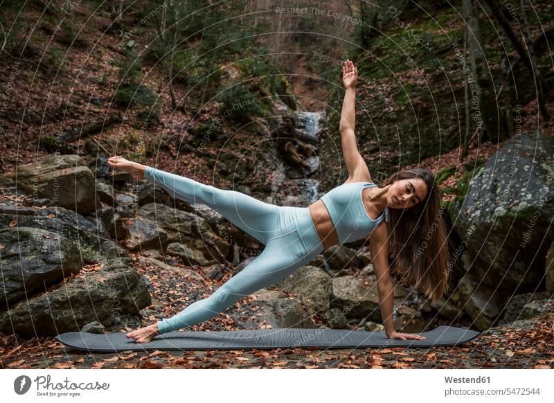 Young woman doing side plank pose on exercise mat against waterfall in forest color image colour image outdoors location shots outdoor shot outdoor shots day