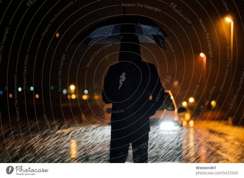 Young man with umbrella standing in front of car dutimng a rainy night color image colour image outdoors location shots outdoor shot outdoor shots