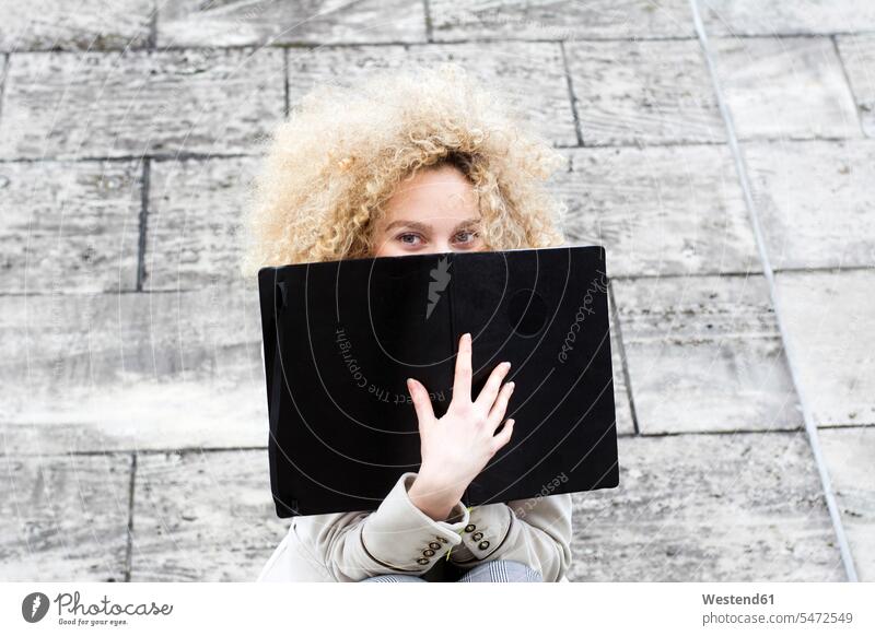 Blond woman with ringlets hiding behind black folder file folders portfolio portfolios files females women blond blond hair blonde hair colour colours Adults